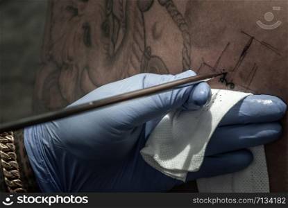 Bangkok, Thailand - 25 Aug 2019 : Tattooing concepts. The artist is tattooing a Thai style pattern on the skin with a pointed metal.