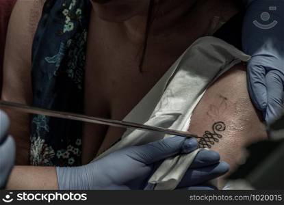 Bangkok, Thailand - 25 Aug 2019 : Tattooing Thai style concepts. Tattoo artist creating a tattoo on a girl&rsquo;s arm with a pointed metal.