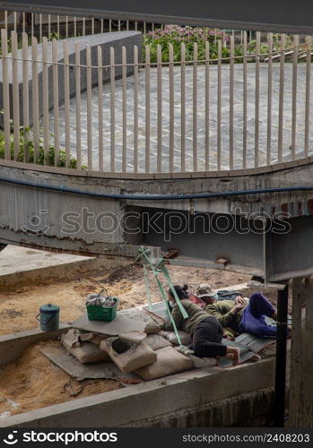 Bangkok, Thailand - Apr 02, 2022   Exhausted tired two construction workers relaxing and fall asleep during working break on the mat under the bridge at a project worksite. Selective focus.