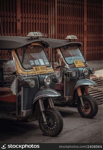 Bangkok, Thailand - Apr 06, 2022 : Famous blue Tuk Tuk or 3-wheeler taxi. Side of Two thai traditional taxi parked in an alley after finishing work, Bangkok street transport, Selective focus.