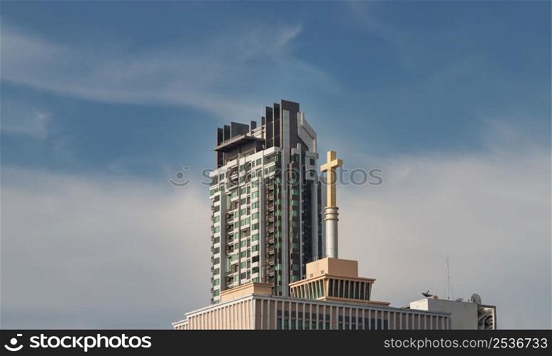 Bangkok, Thailand - Apr 29, 2022 : Urban view overlooking Modern tall building with Christian crucifix on Churches roof against abstract blue sky. Perfectly coexist, Copy space, Selective focus.