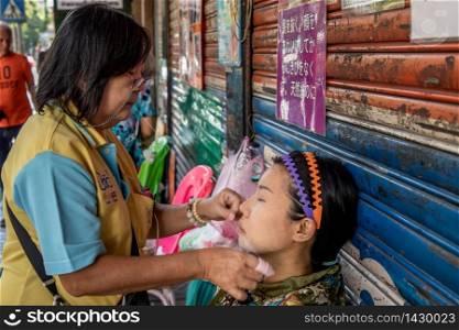 Bangkok, thailand - Feb 16, 2020 : Yaowarat street merchant service customer face hair removal beauty by yarn. Ancient chinese - style hair removal, Chinese traditional ? Mang Ming ? style.