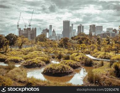 Bangkok, Thailand - Feb 19, 2022 : View of Modern high buildings among green trees space in nature park against blue sky with clouds at afternoon. City growth concept, Selective focus.