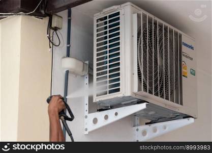 Bangkok, Thailand - July 22, 2017 : Unidentified worker to cleaning coil cooler of air conditioner by water for clean a dust on the wall in customer home when maintenance service. Cleaning air conditioner by water for clean a dust