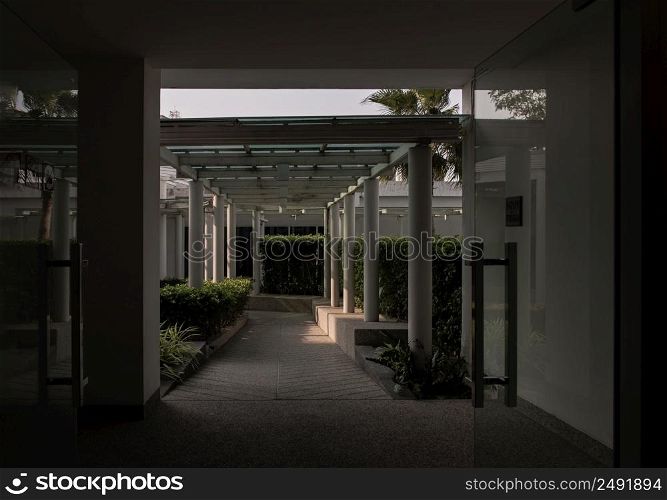 Bangkok,Thailnad - Apr 14, 2022 : The roof and ceiling of the structure is glass and steel. Perspctive view of The stone floor and white concrete pillars leading to an exterior walkway of a garden. Symmetry and geometry, Selective focus.