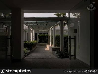 Bangkok,Thailnad - Apr 14, 2022 : The roof and ceiling of the structure is glass and steel. Perspctive view of The stone floor and white concrete pillars leading to an exterior walkway of a garden. Symmetry and geometry, Selective focus.