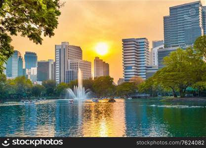 Bangkok view of Lumphini park with beautiful lake with fountain and skyscrapers buildings on skyline at sunset. Bangkok city, Thailand