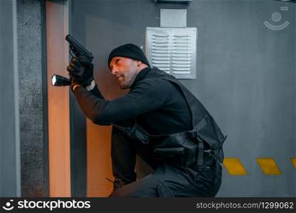 Bank robbery, male robber in black uniform holds gun and lantern. Criminal profession full of risk. Theft of money and jewels concept. Male robber in black uniform holds gun and lantern