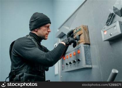 Bank robbery, male robber in black uniform trying to mines the vault door. Criminal profession, theft concept. Robber in uniform trying to mines the vault door