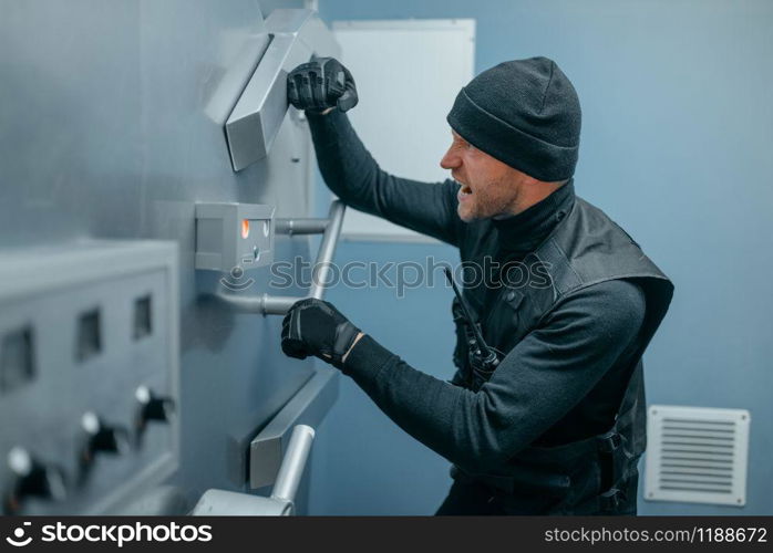 Bank robbery, male robber in black uniform trying to open vault lock. Criminal profession, theft concept. Robbers in black uniform trying to open vault lock