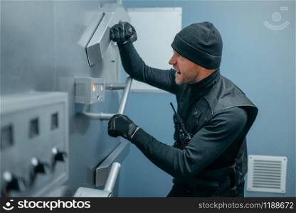 Bank robbery, male robber in black uniform trying to open vault lock. Criminal profession, theft concept. Robbers in black uniform trying to open vault lock