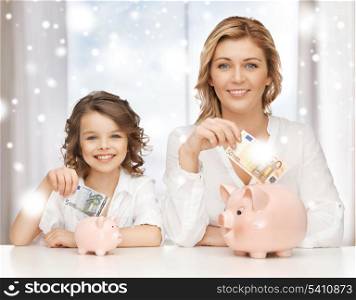 banking, finances, investment and happy people concept - mother and daughter with piggy banks and paper money