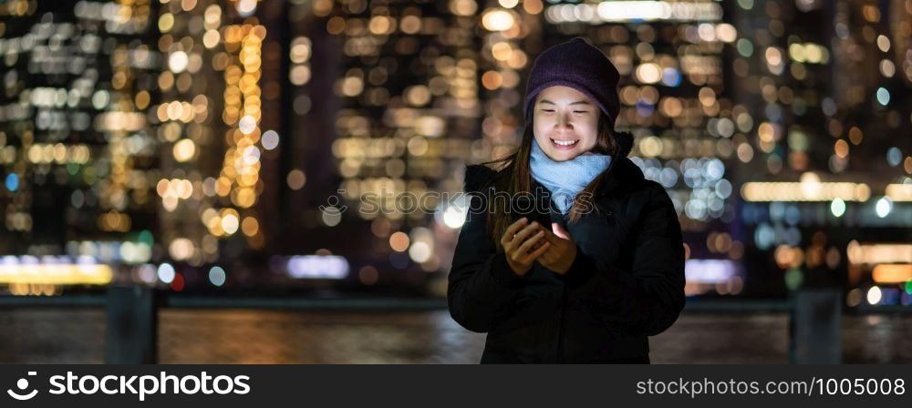 Banner and cover of Asian woman in Winter suit using smart mobile phone with smile action over the photo blurred bokeh of New york Cityscape beside the east river background, USA downtown,
