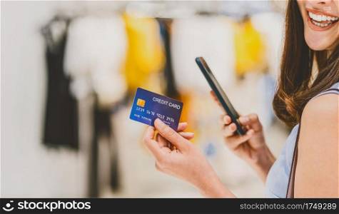 Banner and web page or cover template of Asian woman using credit card with mobile phone for online shopping in department store over the clothes shop store background, credit card mockup