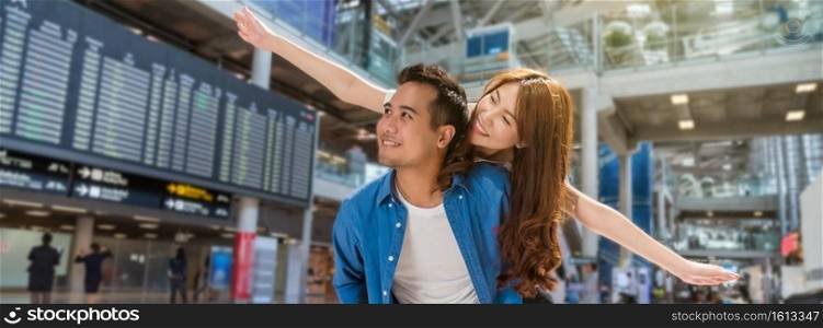Banner and web page or cover template of Happiness Asian couple traveler at the flight information screen in moddern an airport, lifestyle travel and transportation concept.