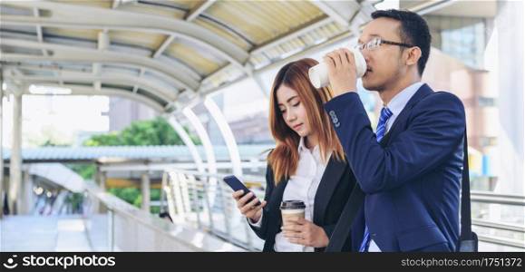 Banner Businessman Businesswoman drinking coffee in town using smartphone outside office city. Panorama Hands holding take away coffee cup, smart phone talking together Business partner copyspace