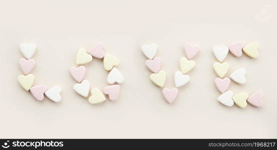 banner inscription love with yellow pink and white candy hearts on a beige background.