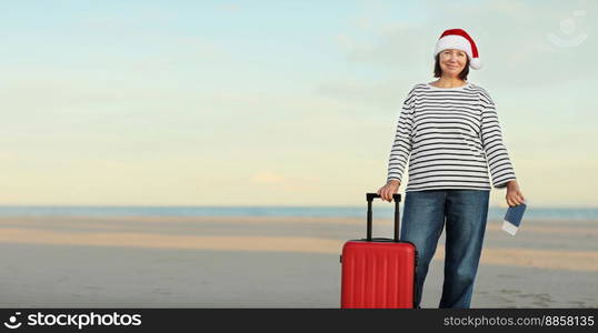 Banner of happy adult woman in Christmas Santa hat with red suitcase, passport boarding pass ticket on beach by the sea background. Happy New Year celebration holiday concept. Winter vacation travel.. Banner of happy adult woman in Christmas Santa hat with red suitcase, passport boarding pass ticket on beach by the sea background. Happy New Year celebration holiday concept. Winter vacation travel