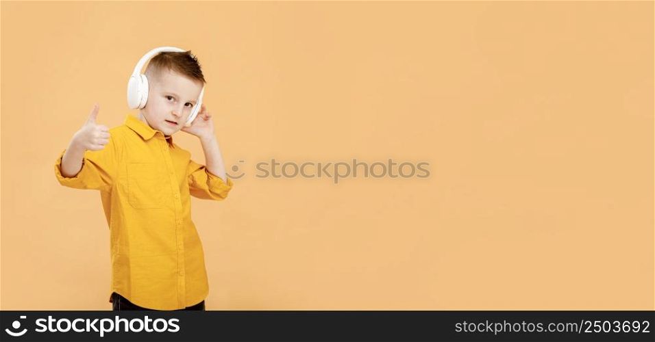 banner of portrait of funny clever school boy with headphones in yellow shirt. Yellow studio background. Education. Looking, smiling and shows a thumb up at camera. High quality photo.. banner of portrait of funny clever school boy with headphones in yellow shirt. Yellow studio background. Education. Looking, smiling and shows a thumb up at camera. High quality photo