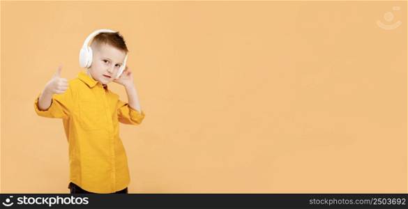 banner of portrait of funny clever school boy with headphones in yellow shirt. Yellow studio background. Education. Looking, smiling and shows a thumb up at camera. High quality photo.. banner of portrait of funny clever school boy with headphones in yellow shirt. Yellow studio background. Education. Looking, smiling and shows a thumb up at camera. High quality photo