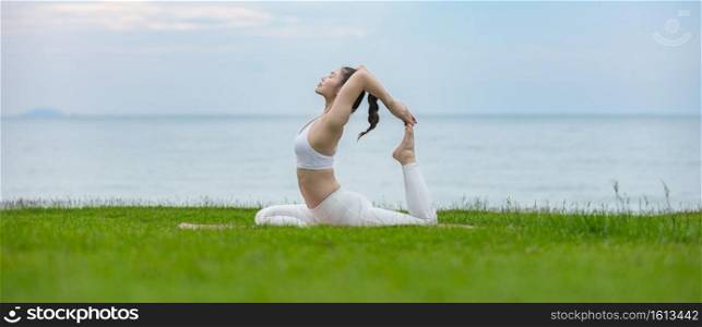 banner of Vacation of Attractive Asian woman relaxing in yoga king pigeon pose on green grass and beach with beautiful sea in Tropical island,Feeling comfortable and relax in holiday,Vacations Concept