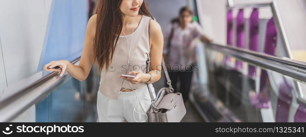 Banner, web page or cover template of Asian woman passenger using smart mobile phone and walking up escalator in subway station when traveling in big city, japanese, chinese, Korean lifestyle concept