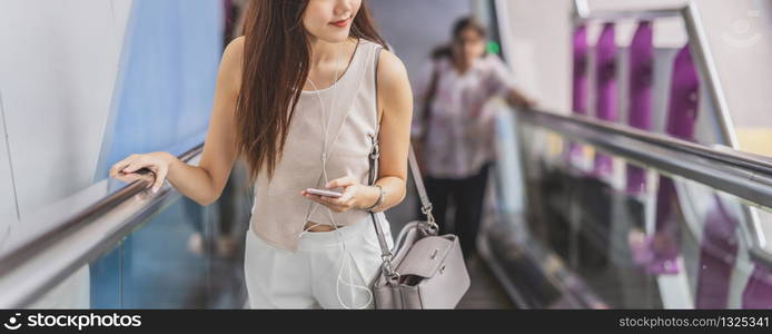 Banner, web page or cover template of Asian woman passenger using smart mobile phone and walking up escalator in subway station when traveling in big city, japanese, chinese, Korean lifestyle concept