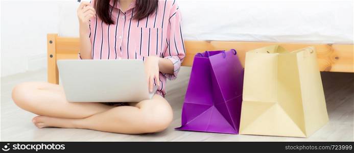 Banner website beautiful asian woman shopping online with laptop computer sitting on floor on room, girl holding credit card purchase and shopping bags, lifestyle concept.