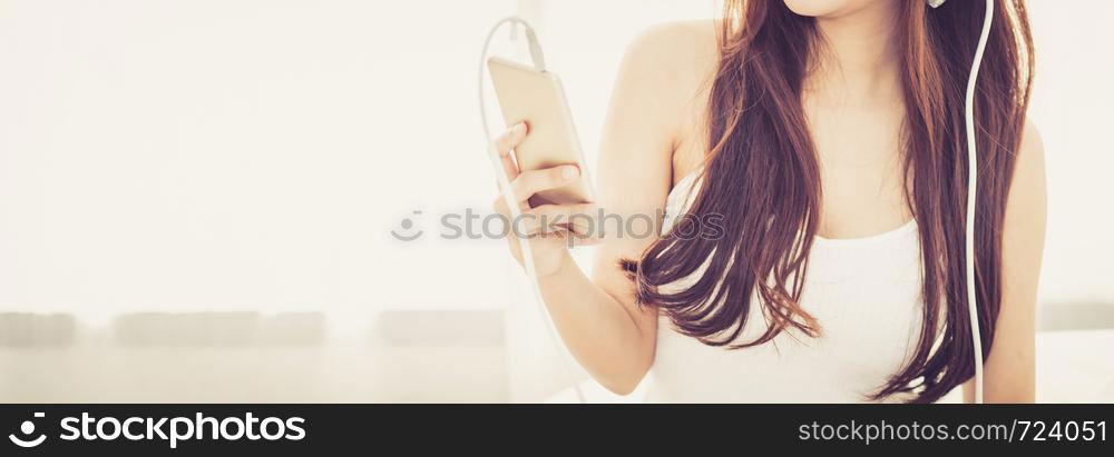 Banner website beautiful asian young woman enjoy listen music with headphone and holding smart mobile phone while sitting in bedroom, relax girl with earphone, leisure and technology concept.