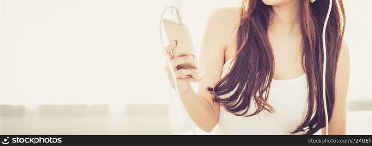 Banner website beautiful asian young woman enjoy listen music with headphone and holding smart mobile phone while sitting in bedroom, relax girl with earphone, leisure and technology concept.