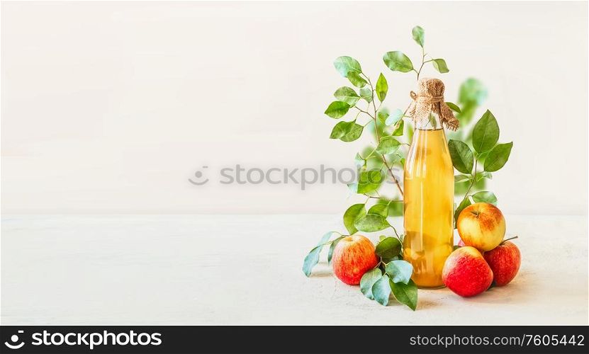 Banner with homemade apple cider vinegar in glass bottle standing on white table with red apples and green leaves at white wall background. Healthy fermented food. Apple preserving