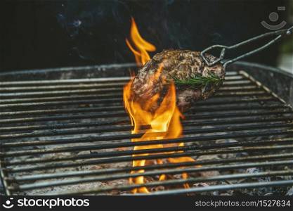 Barbecue hot grilled meat with fire flame heat bbq cooking dinner burn from charcoal. Roast steak grilling with fire and smoking cooking outside. Beef grilling outdoor for party. Western food concept