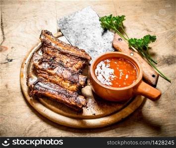 Barbecued ribs with tomato sauce and a carving hatchet. On wooden background.. Barbecued ribs with tomato sauce and a carving hatchet.