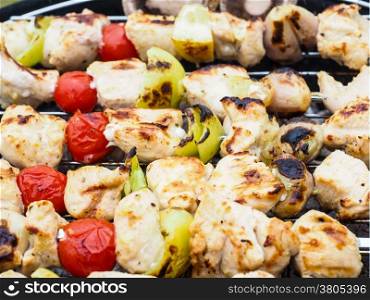 Barbecuing chicken, vegetables on spear over charcoal grill