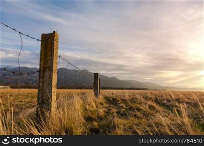 Barbed wired fence on pasture at the sunset
