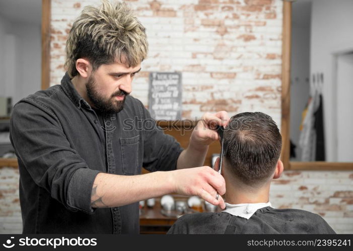 Barber cutting hair with scissors to a handsome young man . High quality photography. Barber cutting hair with scissors to a handsome young man .