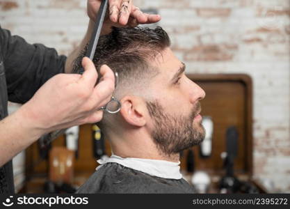 Barber cutting hair with scissors to a handsome young man . High quality photography. Barber cutting hair with scissors to a handsome young man .