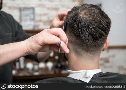 Barber cutting hair with scissors to a handsome young man . High quality photography. Barber cutting hair with scissors to a handsome young man .