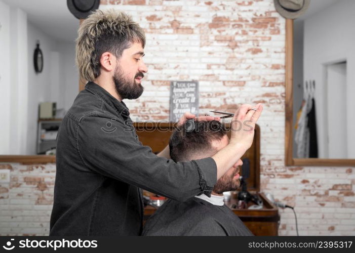 Barber cutting hair with scissors to a handsome young man . High quality photography. Barber cutting hair with scissors to a handsome young man .