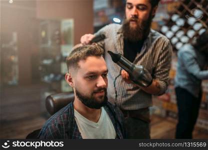 Barber dry the client&rsquo;s hair with hairdryer. Hairdressing salon interior on background