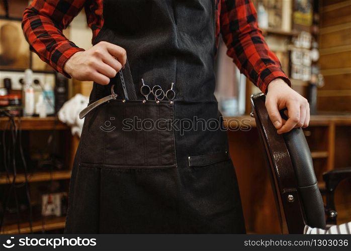 Barber, focus on apron with cutting tools. Professional barbershop is a trendy occupation. Male hairdresser in retro style hair salon, accessories. Barber in apron with cutting tools, barbershop