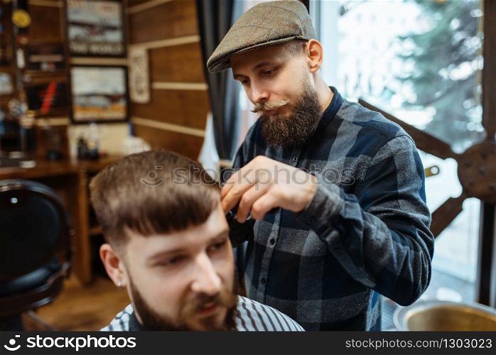 Barber holds comb and cuts the client &rsquo;s hair. Professional barbershop is a trendy occupation. Male hairdresser and customer in retro style salon. Barber holds comb and cuts the client &rsquo;s hair