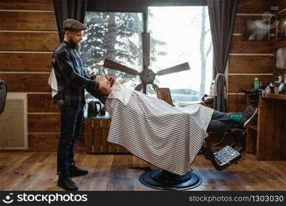 Barber in hat and bearded customer, beard cutting. Professional barbershop is a trendy occupation. Male hairdresser and client in hair salon. Barber in hat and bearded customer, beard cutting