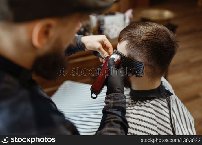 Barber in hat cuts the client &rsquo;s hair. Professional barbershop is a trendy occupation. Male hairdresser and customer in retro style hair salon. Barber in hat cuts the client &rsquo;s hair, barbershop