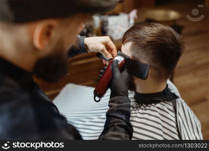 Barber in hat cuts the client &rsquo;s hair. Professional barbershop is a trendy occupation. Male hairdresser and customer in retro style hair salon. Barber in hat cuts the client &rsquo;s hair, barbershop