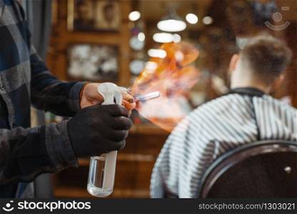 Barber processes the blade with fire, customer sitting in chair. Professional barbershop is a trendy occupation. Male hairdresser and client in hair salon. Barber processes the blade with fire, barbershop