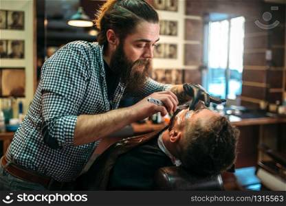 Barber shaves the beard of the client by shaving blade at barbershop.
