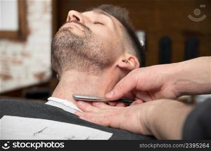 Barber shaving bearded male with a sharp razor. High quality photography. Barber shaving bearded male with a sharp razor