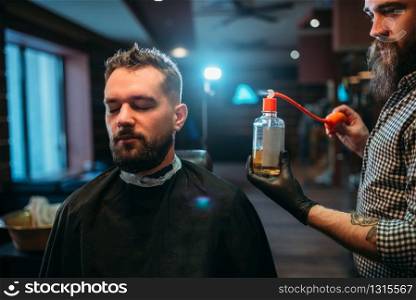 Barber splashing client face by aftershave lotion, barbershop interior on background.