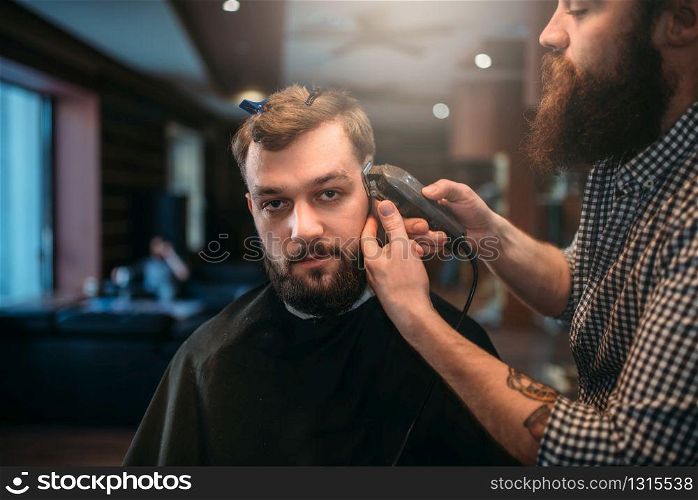 Barber trimming hair of the client man by clipper. Barbershop concept